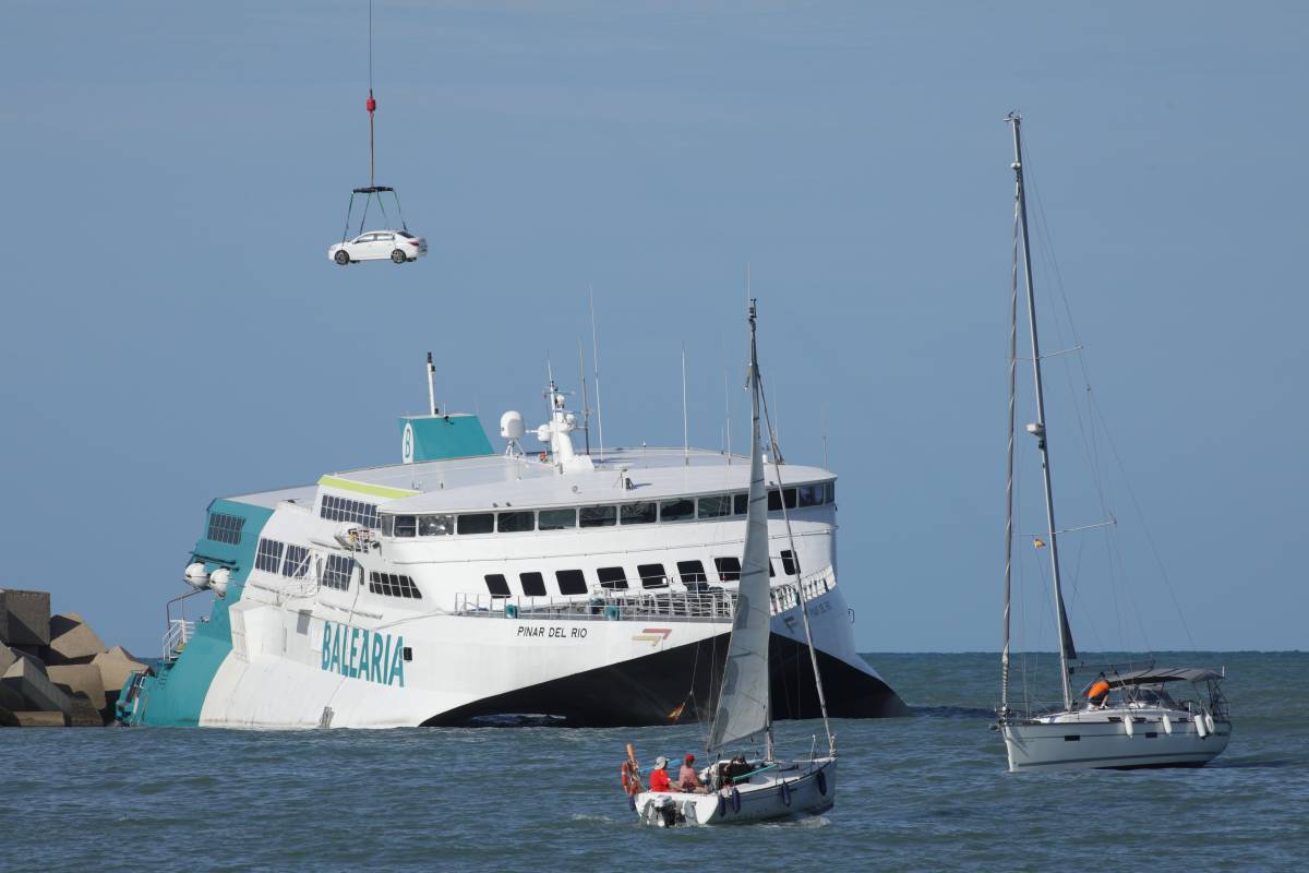 Dos embarcaciones siguen la descarga de vehículos de la bodega del ferry. Foto: EFE