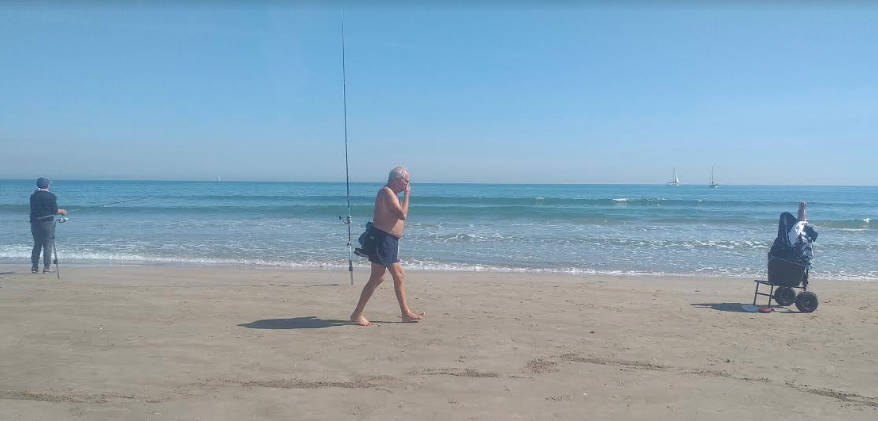 Un hombre pasea tranquilo por la playa mientras otro pesca, indiferentes al clima de histeria general.