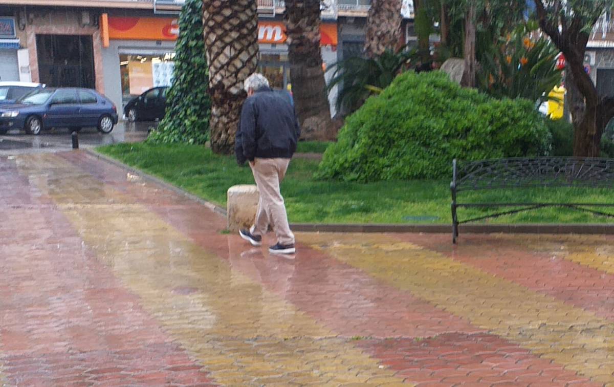 Un hombre pasea por la plaza de un pueblo mientras llueve.